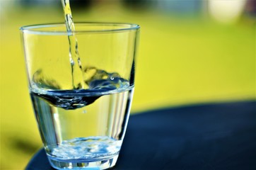 Water poured into transparent glass, green background, writing space, healthy lifestyle, wave, laminar liquid, drop