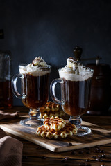 Two cups of coffee with whipped cream and grated chocolate on a dark concrete background. Viennese coffee with Viennese waffles.