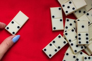  Play dominoes. A female hand lays domino bones on a red cloth next to a bunch of dominoes.