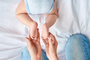Baby Care. Young mother holding feet of little son in her hands top view close-up