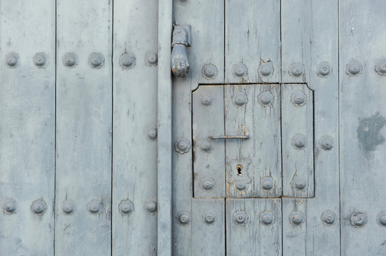 Aged gray wooden door with lock, knocker and window of a house in a Spanish village. Textured background