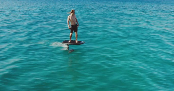 Young thrill seeking adventurous man riding fast on an electric hydrofoil in blue ocean water, the future of green renewable water craft technology is here with the invention of electric hydrofoils