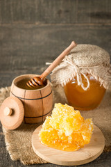 Honey dripping from a wooden honey dipper in a jar on wooden grey rustic background