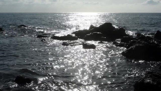 Reflejos del sol provocan estrellas sobre el agua del mar, las olas se mueven entre peque&ntilde;as rocas de un arrecife