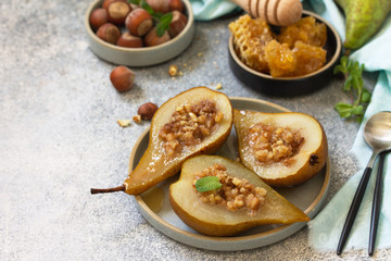 Healthy diet dessert. Baked pears with hazelnuts, honey and granola on a slate, stone or concrete background. Copy space.