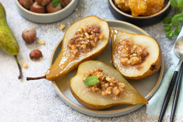 Healthy diet dessert. Baked pears with hazelnuts, honey and granola on a slate, stone or concrete background.