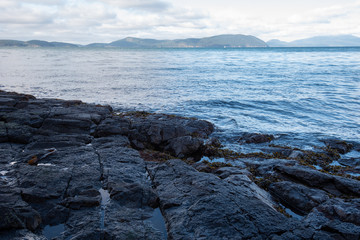 Landscape of black horizontal rocks, the Pacific Ocean and distant islands in Anacortes, Washington