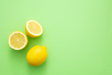 Ripe lemons on green color background. Whole yellow lemon citrus fruit and lemon cut half, top view, copy space