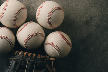 Group of baseballs with glove on dark background, close up flat lay