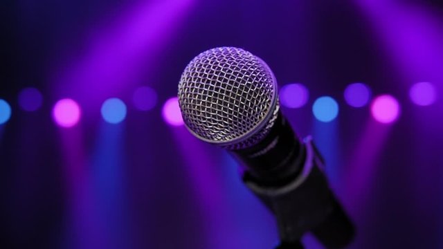 Close-up of microphone on stage in the dark against the background of multicolored lights of concert lighting. Slow motion.