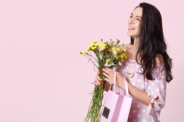 Horizontal studio shot of cheerful magnetic positive female looking aside, wearing dress, smiling...