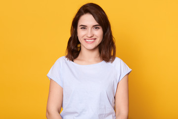 Fototapeta premium Head shot portrait of young woman having wide white smile, wearing white t shirt, lady looking at camera, pretty female posing isolated over bright yellow background, girl expressing happyness.
