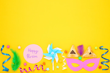 Purim holiday composition. Cookies with party supplies and text Happy Purim on yellow background