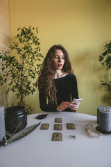 beautiful young woman in a black corduroy dress is guessing on cards with runes and uses an online...