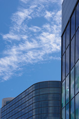 Low angle partial view of the glass facades of some large corporate office buildings with a blue sky with some cirrus clouds above