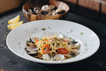 Pasta with clams on white plate on black background. Mediterranean delicacy food. Flat lay. Top view