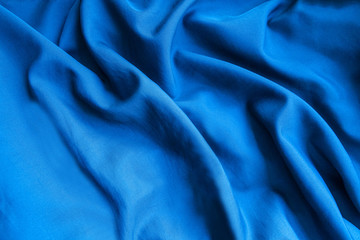 Blue satin fabric. Silk textile background. Wavy folds of material.