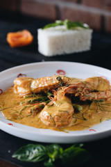 Prawns in Curry sauce on white plate on black wooden background. Top view