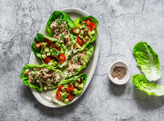 Leaves of mini roman salad stuffed with tuna, egg, tomato, avocado on a gray background, top view....