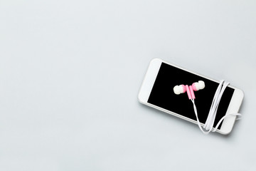 Earphones with mobile phone on grey background