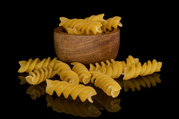 Lot of whole yellow pasta fusilli in bamboo bowl isolated on black glass