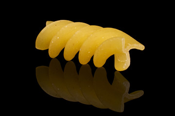 One whole yellow pasta fusilli isolated on black glass
