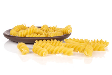 Lot of whole uncooked yellow pasta fusilli with brown ceramic coaster isolated on white background