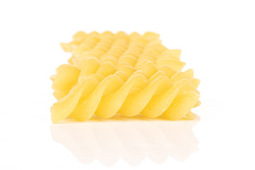 Lot of whole yellow pasta fusilli in row isolated on white background
