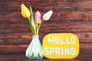 Tulip flowers in vase with text Hello Spring on brown wooden background