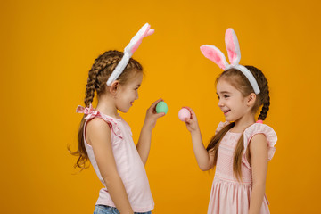 happy cute little child girls with pink bunny ears holding painted Easter eggs on studio yellow background. Easter day