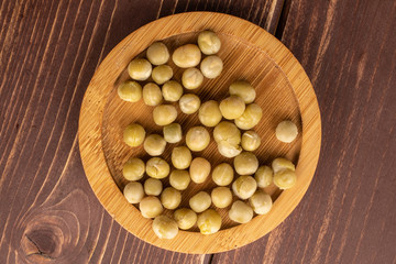 Lot of whole canned pea on round bamboo coaster flatlay on brown wood