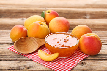 Jam in bowl and apricots on brown wooden table