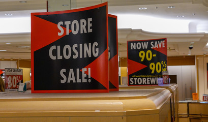 Signs for a store closing bankruptcy sale on top of a display case. Signs indicate 90% off