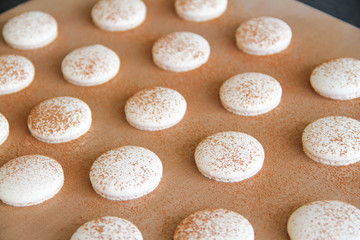 Fototapeta na wymiar French dessert macaron. The photo of making macaron powdered with cocoa powder. Macaron in process, after baking, before filling. Macarons piped on a tray covered with a teflon sheet. Back view.