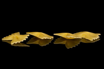 Naklejka premium Group of four whole uncooked yellow pasta farfalle isolated on black glass