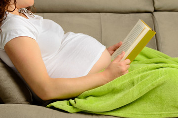 pregnant woman reading a baby book at home