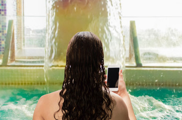 woman relaxing and looking at a phone in the pool in a spa center