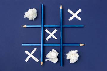 Tic Tac Toe is made of pencils and paper. Blue pencils on a blue background. Crosses from paper,...