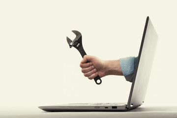 The human hand with  black wrench stick out of a laptop screen. Concept of technical support. - obrazy, fototapety, plakaty