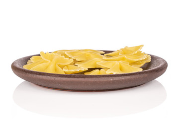 Lot of whole yellow pasta farfalle with brown ceramic coaster isolated on white background