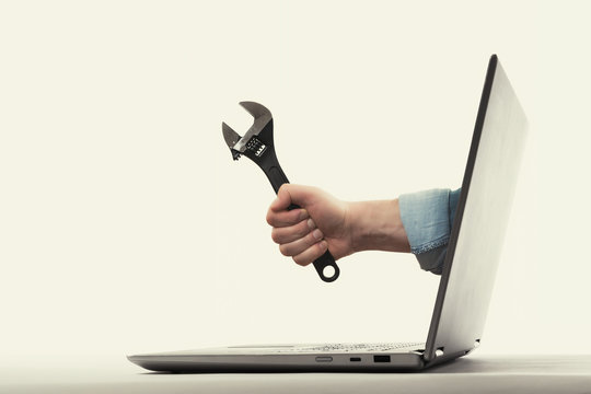 The human hand with  black wrench stick out of a laptop screen. Concept of technical support.