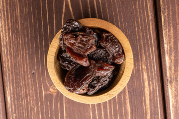 Lot of whole dried dark raisin in bamboo bowl flatlay on brown wood