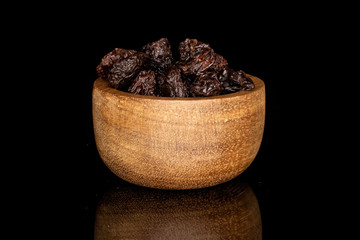 Lot of whole dried dark raisin in bamboo bowl isolated on black glass