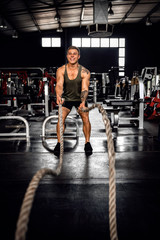 Fototapeta na wymiar Smiling young man exercising with battle ropes in a gym