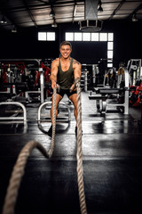 Fototapeta na wymiar Fit young man smiling while working out with battle ropes