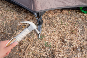 Hammer putting a nail-like tent peg out of iron into the grass on the ground. Push the anchor of the tent onto the ground.Travel concept.