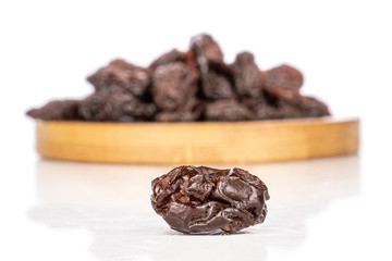 Lot of whole dried dark raisin one in front on round bamboo coaster isolated on white background