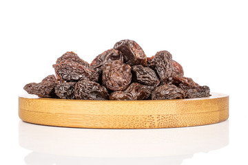 Lot of whole dried dark raisin on round bamboo coaster isolated on white background