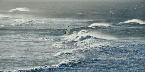Panoramic view of the ocean with windsurfer among the waves on a windy day on Maui island in Hawaii.