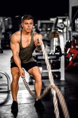 Fototapeta na wymiar Muscular young man using battle ropes during a gym workout